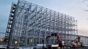 Steel structure framework of a commercial building under construction with cranes and equipment on site.